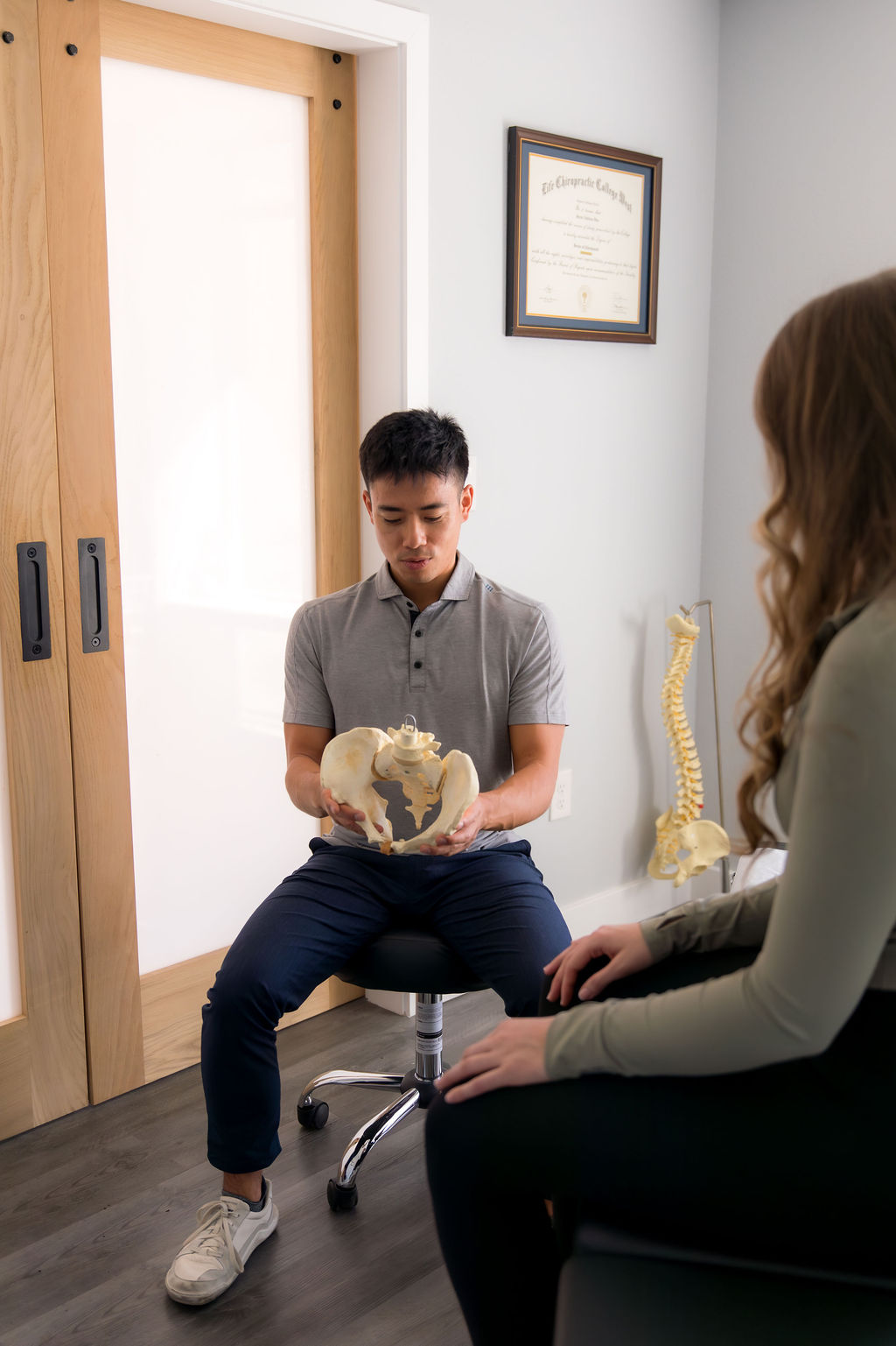 Dr. Jaron Hua explaining a pelvis model to a seated patient at G3 Chiro in Newport Beach